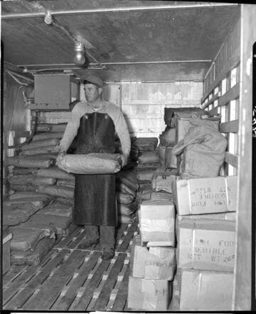 Man storing sacks of ground meat products in cold storage. Sacks are marked "fish food