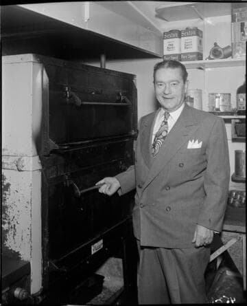 Man in suit standing next to commercial electric oven in restaurant kitchen