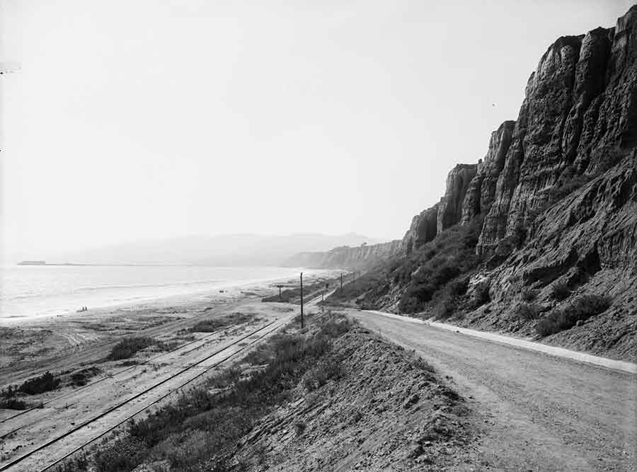 Glass plate negative, made ca. 1905–10, showing what is now the California Incline road leading down to the beach and railroad tracks in Santa Monica. The Southern Pacific Railroad ran steam engines along these tracks between Los Angeles and the Long Wharf, seen in the distance at left. Unidentified photographer.